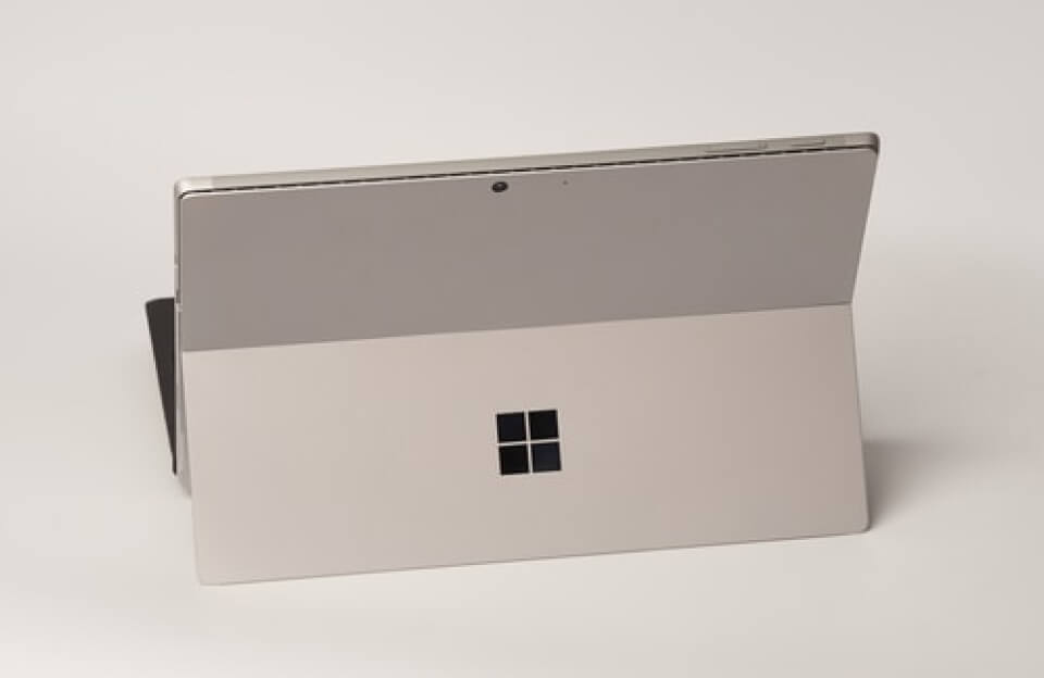 جهاز Microsoft Surface باللون الفضي يعرض بزاوية على سطح أبيض مع ملامح تصميم معدني نظيف وكاميرا أمامية صغيرة في الأعلى.