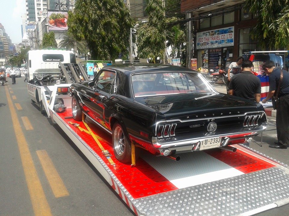 سيارة كلاسيكية سوداء على شاحنة سحب في شارع مزدحم مع أشخاص في الخلفية.